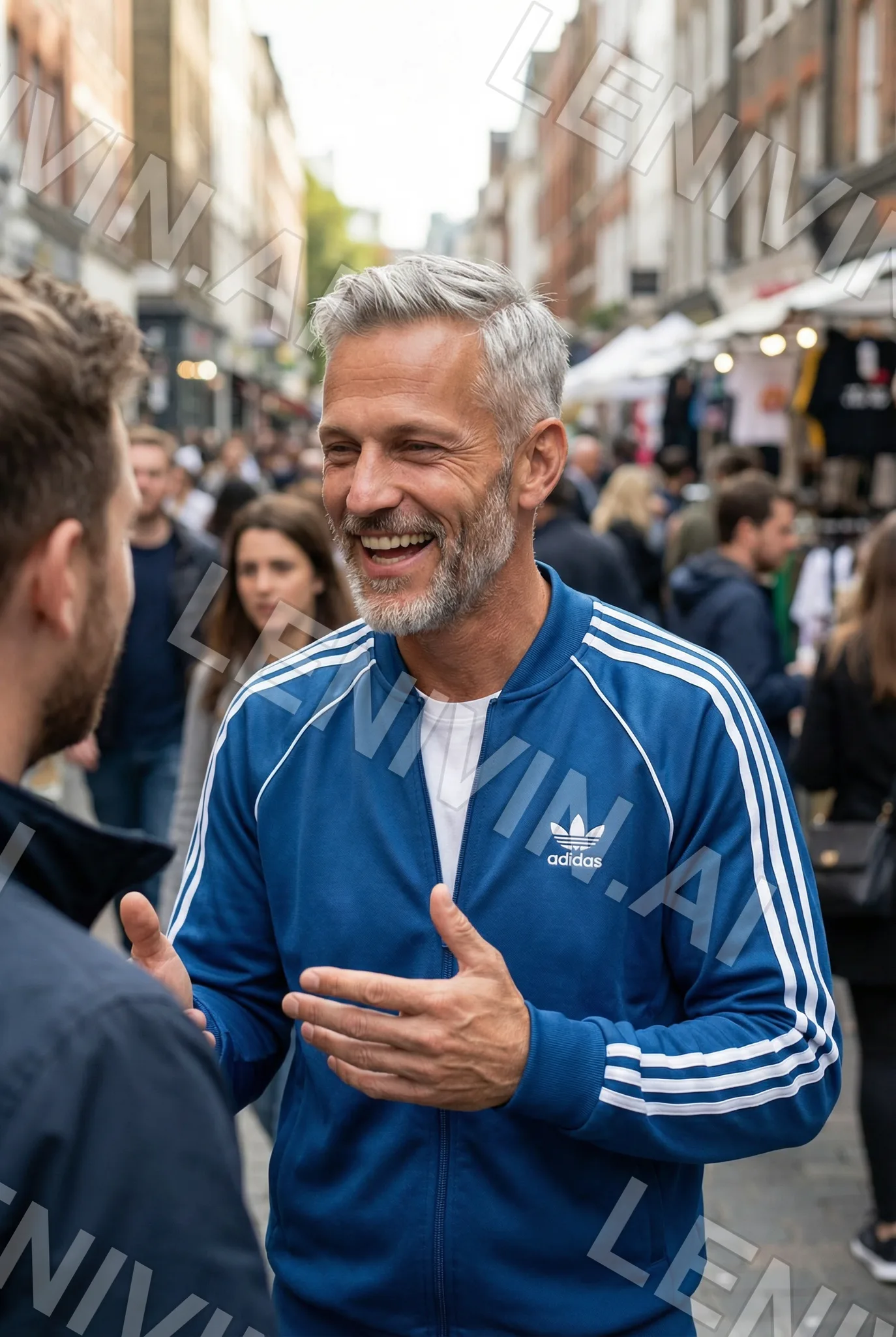 Смеющийся седой мужчина в синей олимпийке Adidas разговаривает на людной рыночной улице