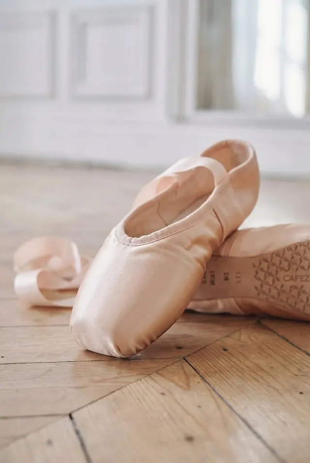 Персиковые атласные пуанты Capezio на паркете, мягкий дневной свет, светлый зал