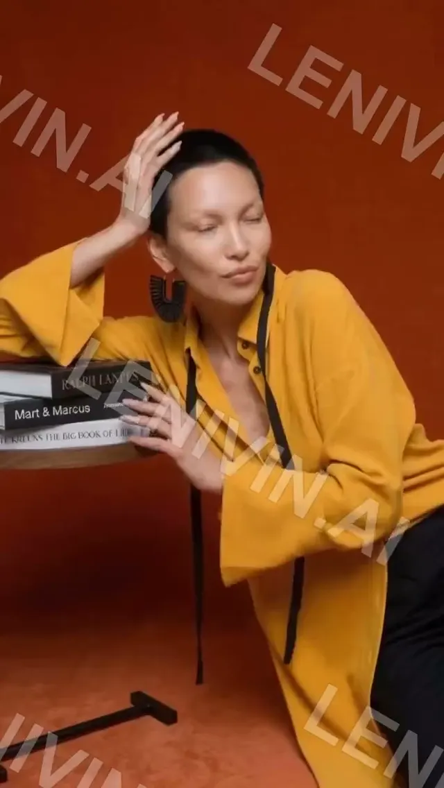 Ролик: женщина в жёлтом жакете облокотилась на столик с книгами на красно-оранжевом фоне