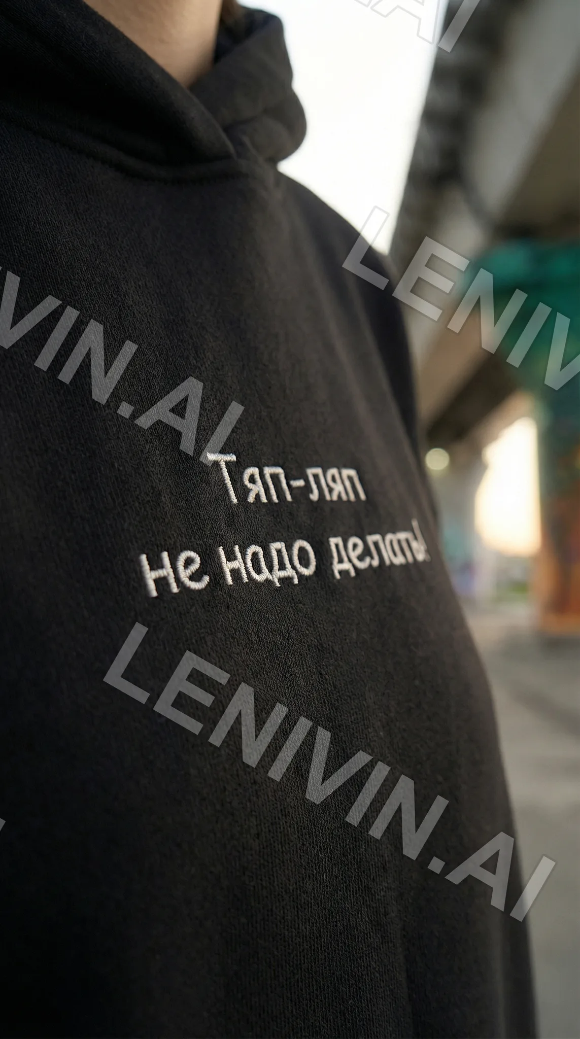 Чёрная худи крупно с вышитой надписью «Тяп-ляп не надо делать», размытый городской фон